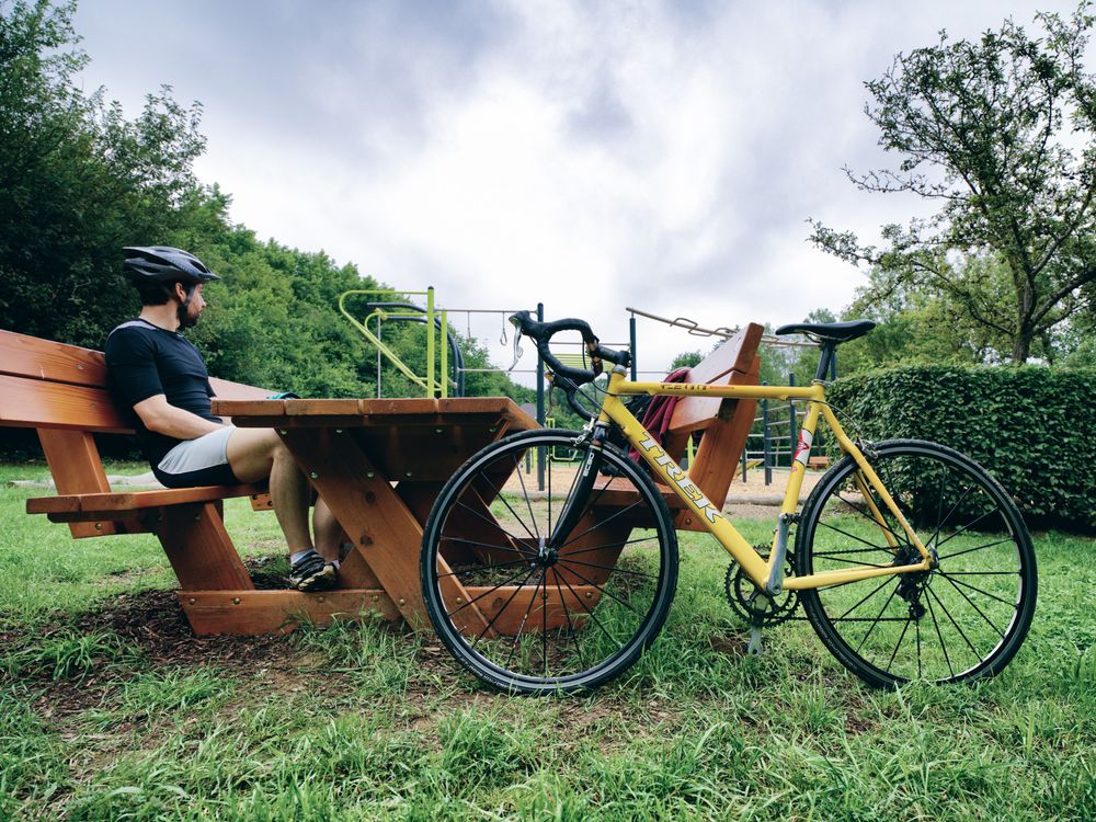 Un cycliste fait une pause sur un banc de parc; son vélo jaune est garé vers l'avant