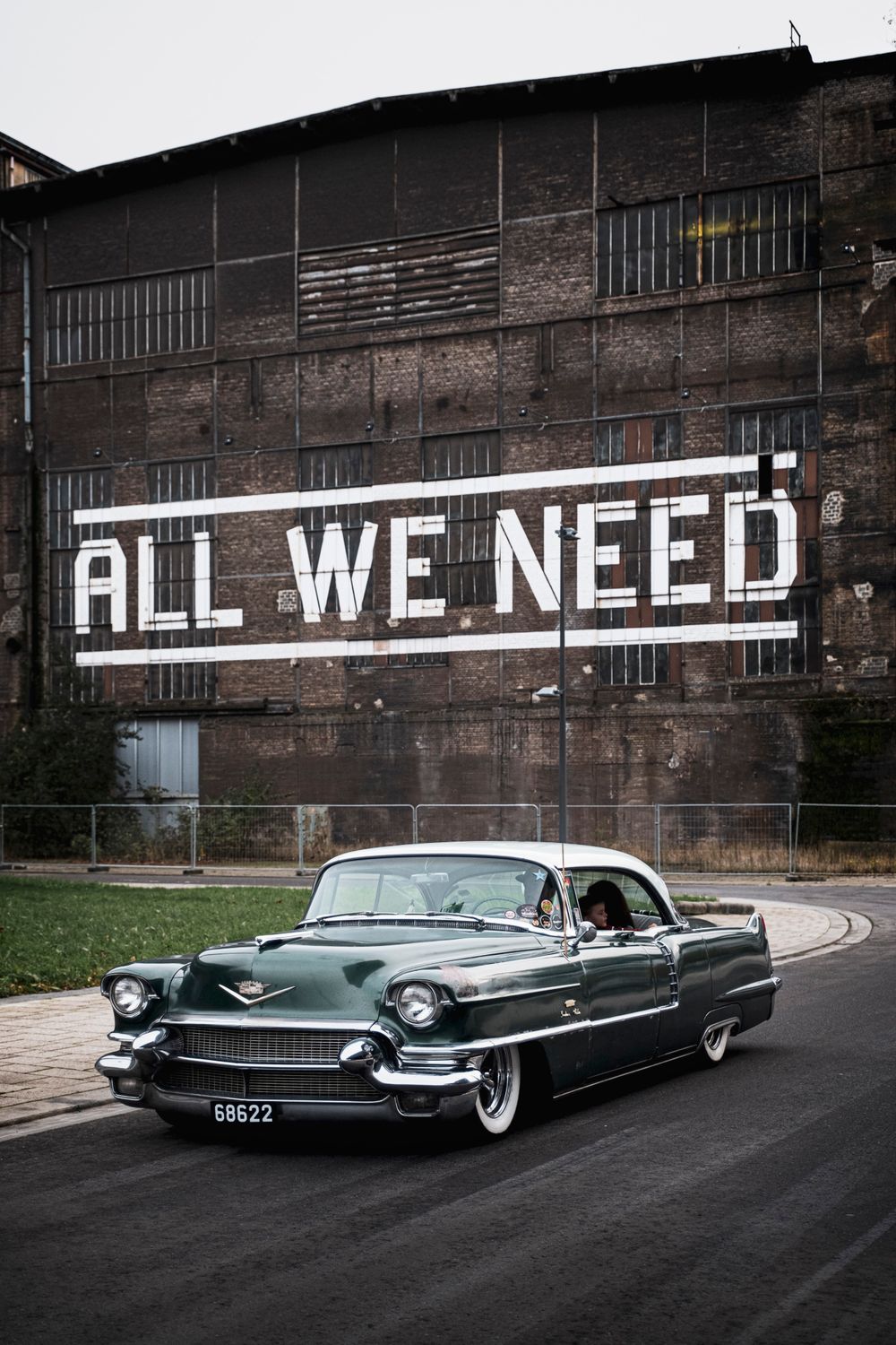 Ein Oldtimer unterwegs auf der Straße vor einer alten Industriehalle auf Belval. Auf der Halle steht in großen Lettern "All we need"