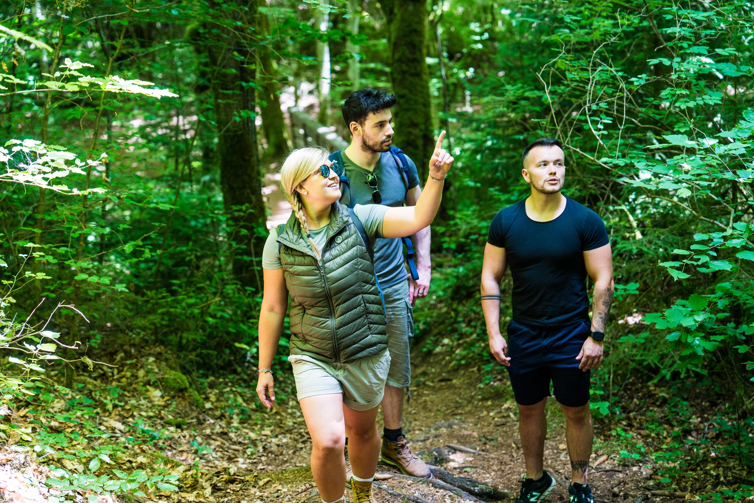 Une jeune randonneuse semble expliquer quelque chose à son groupe de randonneurs alors qu'ils marchent le long d'un sentier forestier.