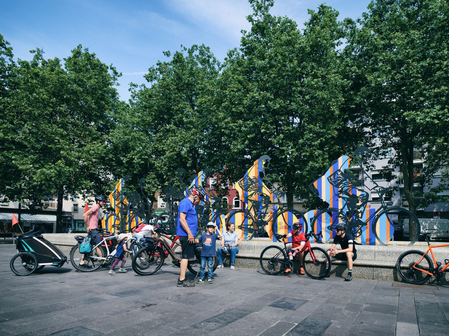 Groupe de cyclistes dans l'espace public, devant une œuvre d'art censée représenter un groupe de cyclistes