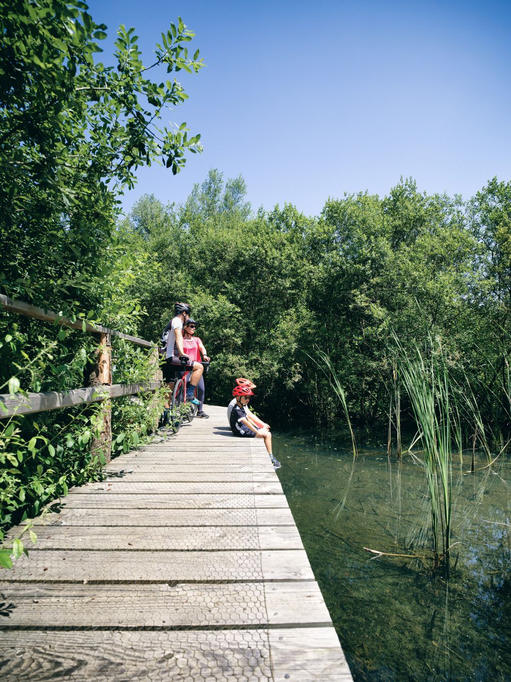 Une famille en balade à vélo fait une pause sur un pont en bois au-dessus d'un ruisseau.