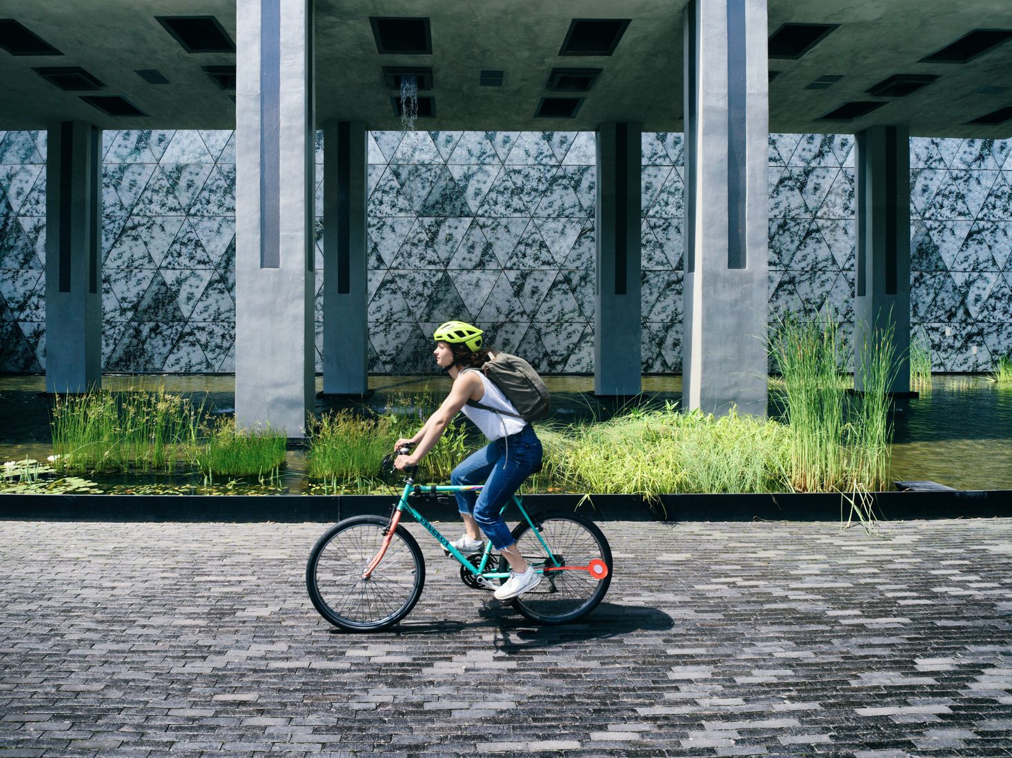 Eine Dame auf ihrem Fahrrad auf den Pflastersteinen des Belval; im Hintergrund Teile der alten Industrieanlage