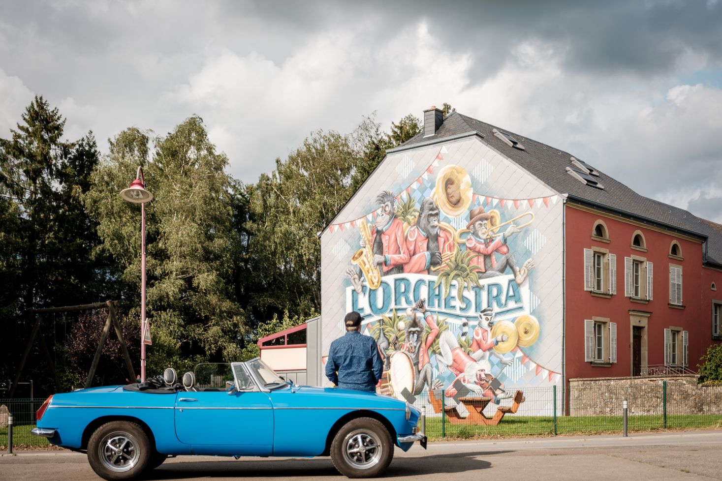 Ein Mann betrachtet eine große Wanddekoration während einer kurzen Pause auf seinem Road Trip. Er lehnt sich auf die Motorhaube seines blauen Oldtimers